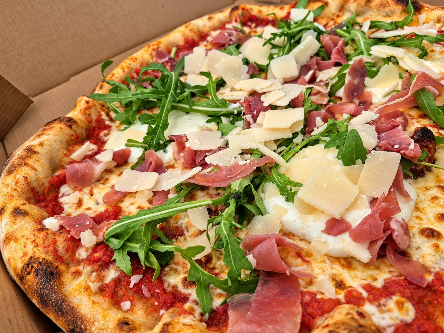 Pizza maison garnie de burrata, roquette, jambon cru et parmesan